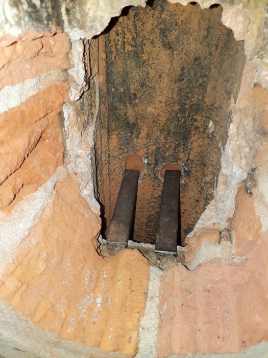 Fyrkantiga rör och en metallplåt används i en murad skorsten, med synligt bruk, redo för sotarens inspektion.