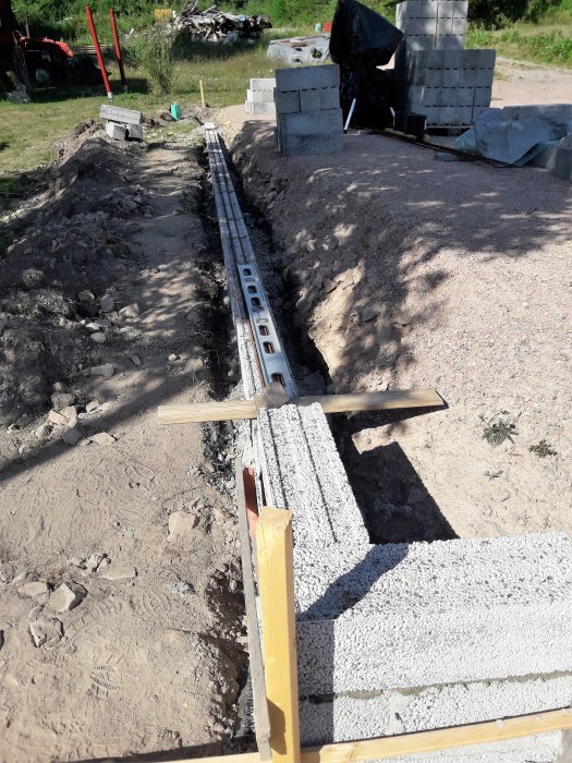Grundarbete för verkstad med synlig dräneringsrör och hög av betongblock vid en byggarbetsplats.