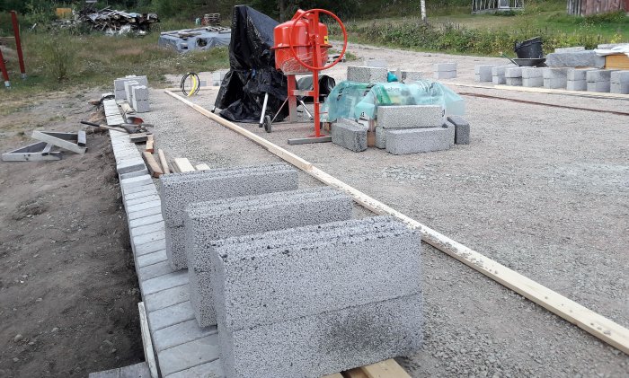 Uppförande av en mur med lättbetongblock vid ett verkstadsbygge, med betongblandare och byggmaterial synligt.