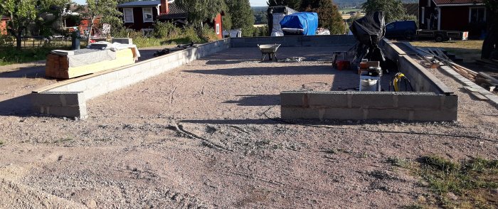 Betonggrund för verkstadsbygge med murblock och byggmaterial på grusunderlag.