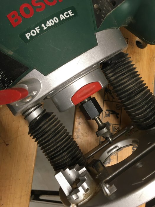 Bosch POF 1400-fräs fastnat i fräsbord, inzoomad på låsknappen och frässtålet.