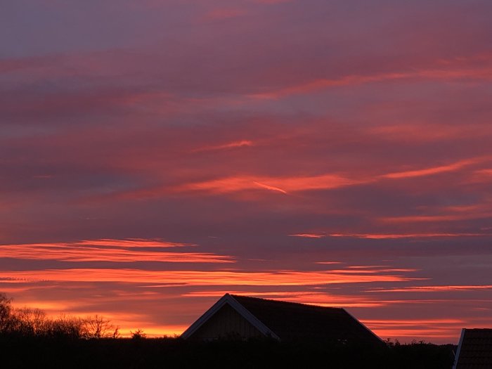 Solnedgång med dramatiska rosa och orange moln bakom silhuetten av ett hus.