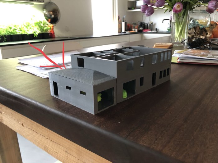 3D-utskriven modell av ett hus med utbyggnad och sluttande tak placerad på ett bord.