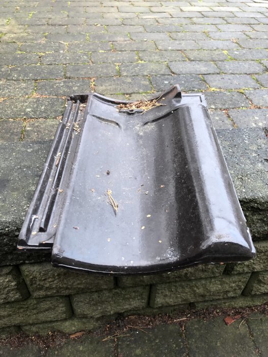 Svart enkupig takpanna placerad på markstenar, smuts och löv syns på ytan.