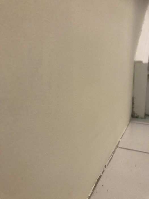 Ojämnt spacklad och målad källarvägg med synliga defekter vid övergång till klinkergolv.