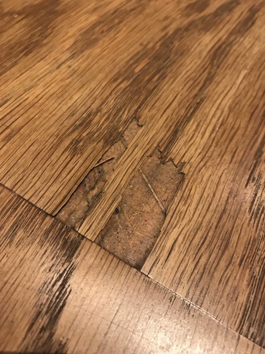 Skadat golv med tunt översta lager och fuktfläckar synliga, möjligt laminat.