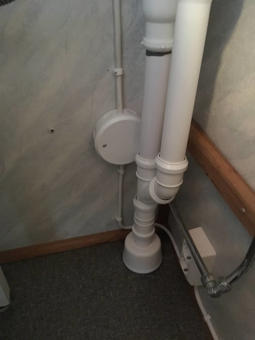 Nyligen installerade vita avloppsrör längs en vägg med dragning över golvkanten.