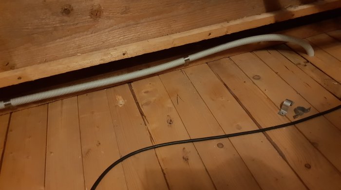 Flexrör för installation av nätverkskabel, draget längs en träbjälke med klammer och böjningar vid ändarna.