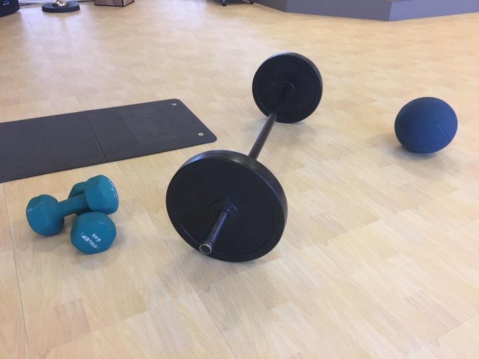 Gymutrustning på Bergo golv med hantlar, barbell och medicinboll.
