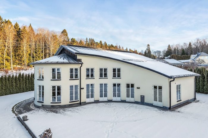 Stort tvåvåningshus med ovanlig design täckt av snö, beläget i ett snöigt landskap.