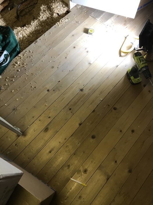 Renoveringsprojekt med gammalt trätak, mätverktyg och borr på golvet.