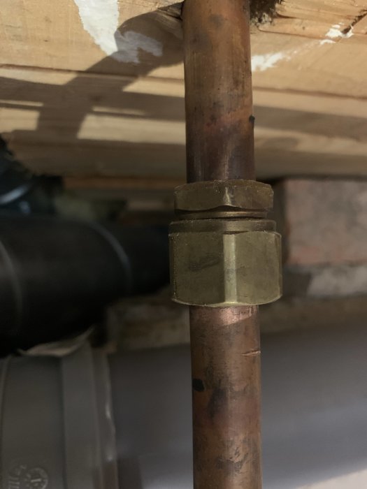 Gammal 16mm kopparrör med en äldre klämring monterad, under en träbjälke.