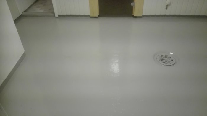 Nymålat grått betonggolv med avloppsgaller, omgivet av vita väggar och dörröppningar.