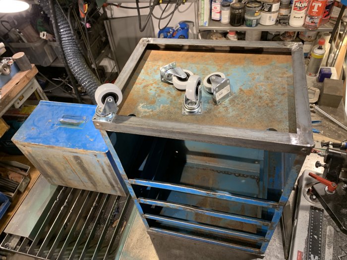 En upcyclad blå verktygshurts med öppna lådor och nytillagda vita hjul på en verkstadsbänk, visar DIY förvaringsprojekt.