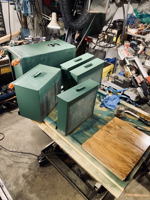 Renoverade verktygslådor i grönt med handtag, hjul och träbit på en arbetsbänk i en verkstad.