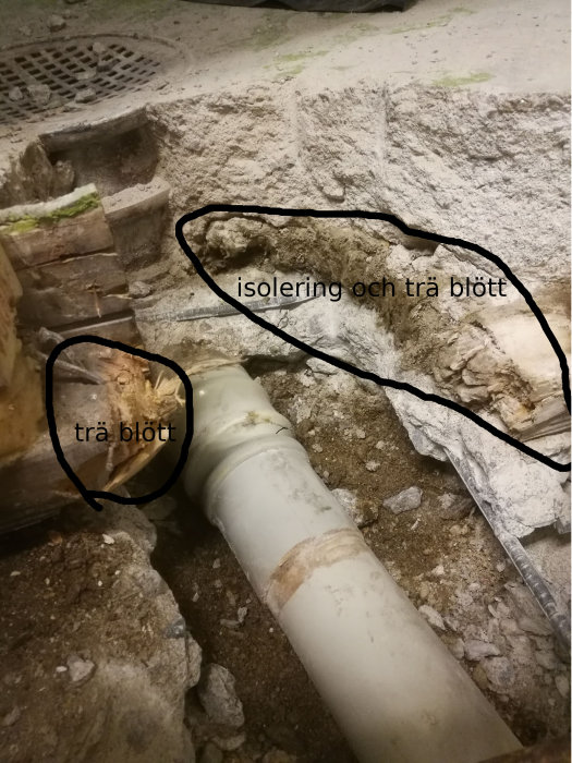 Grund med synligt avloppsrör, fuktig mineralullisolering och träbjälke i en uppgrävd del av en villa från 1971.