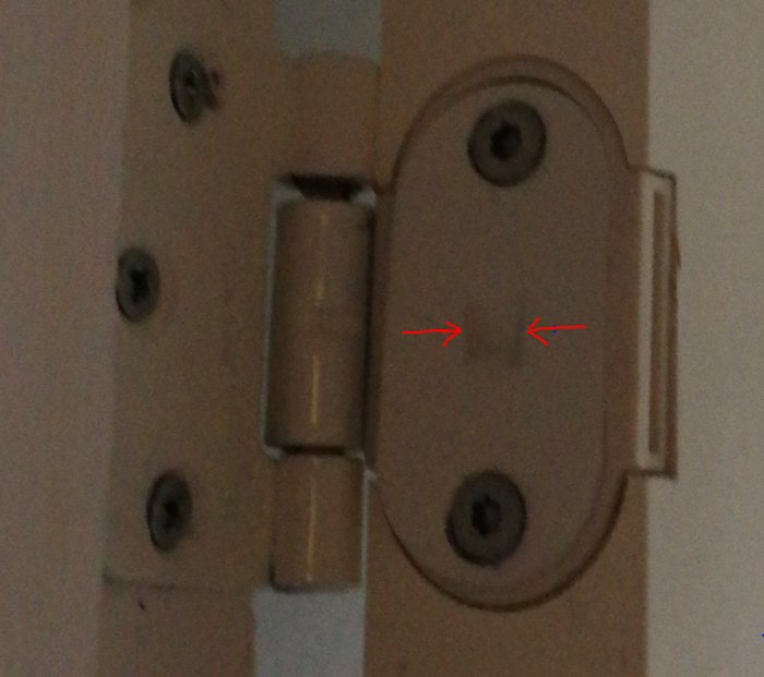 Närbild av en dörrvårt med röda pilar som pekar på en fyrkantig plåt mot en gångjärnsflärp.