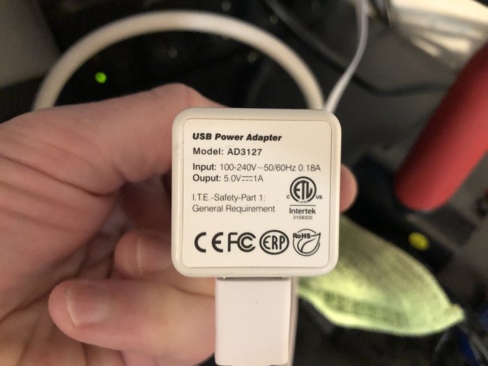 Hand håller en USB-strömadapter med specifikationer synliga, använd för mikrofon till övervakningskamera.