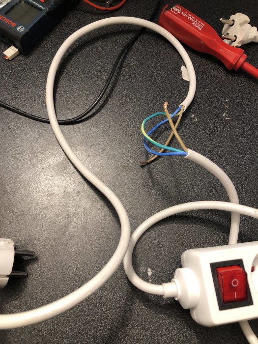 Öppnat grenuttag med exponerade kablar och mätinstrument på ett arbetsbord.