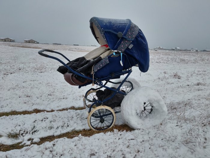 En barnvagn med stora hemmagjorda vinterdäck av snö står på ett snötäckt fält.