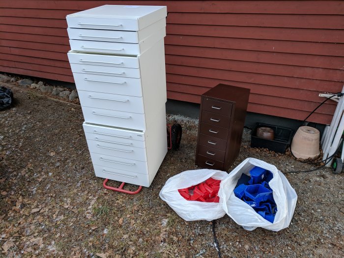 Vit högkvalitativ förvaringslådor och brun metall-hutch med blå och röda plastdelar i påsar framför röd vägg.