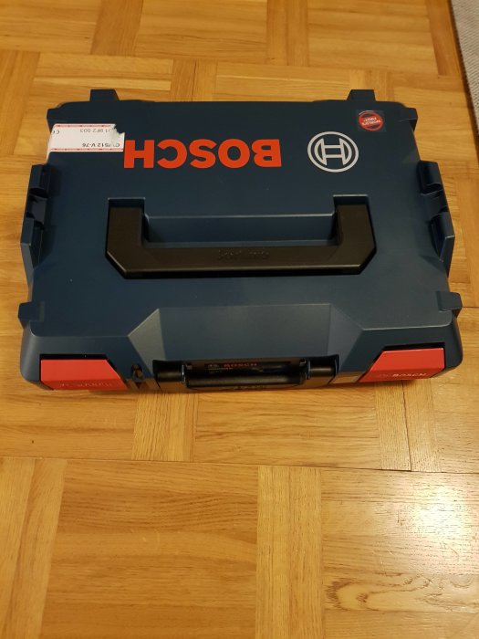 Stängd blå och röd Bosch verktygslåda på trägolv med prislapp.