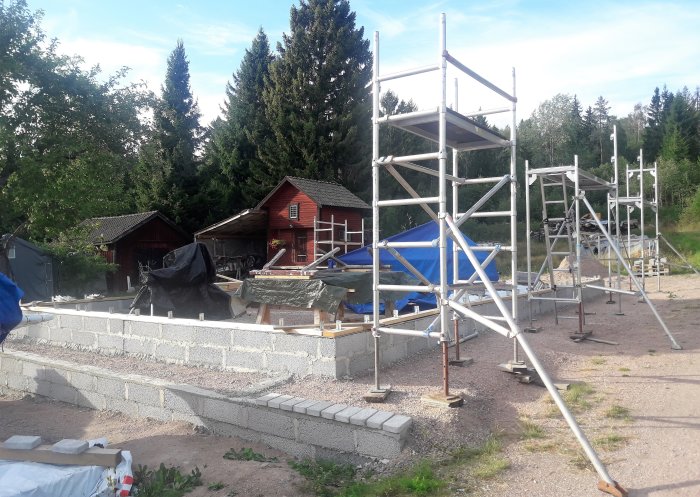 Konstruktionsplats med byggställningar och grundstommen till ett tak med skyddande presenning på en gård.