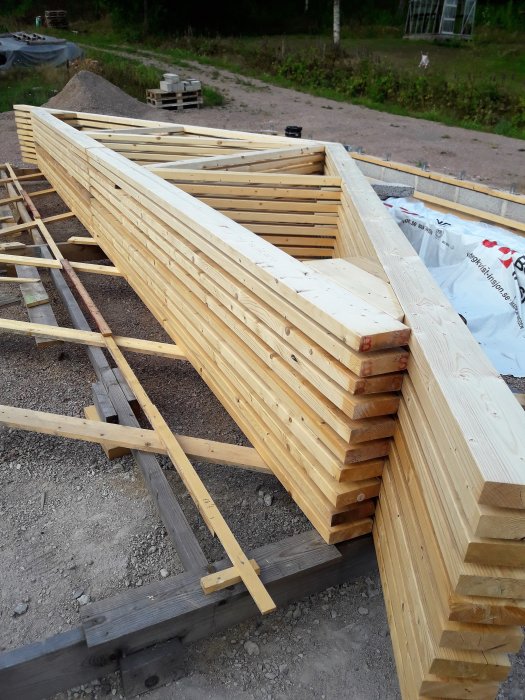Stapel med nykapade trästolpar och balkar för byggnadsstomme med märkning och stödben på grusunderlag.