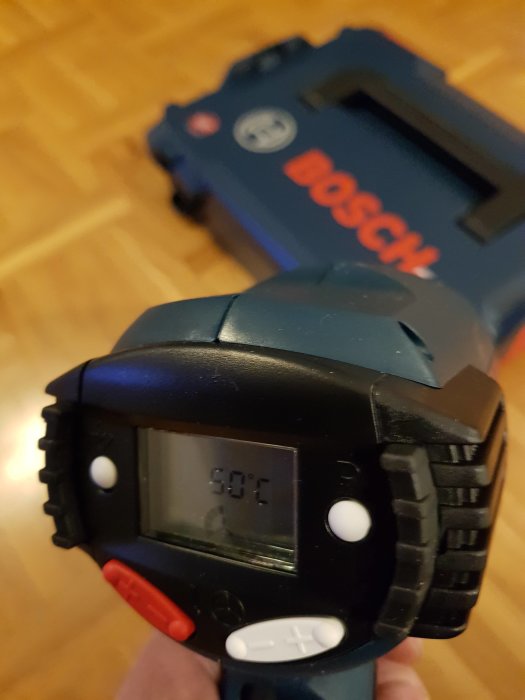 Närbild av en Bosch GHG 660 LCD varmluftspistol som visar en LCD-skärm med temperaturen 500 grader Celsius, med ett suddigt fodral i bakgrunden.