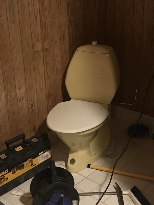 Gult Ifö-toalett i ett badrum under renovering med verktyg och byggmaterial runtomkring.