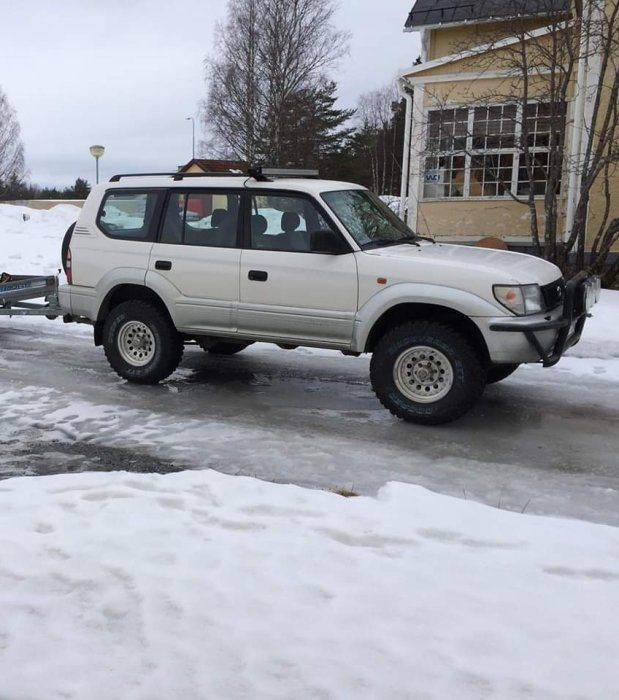 Vit Toyota Landcruiser parkerad på snöklädd väg, utan synligt extraljusfäste.