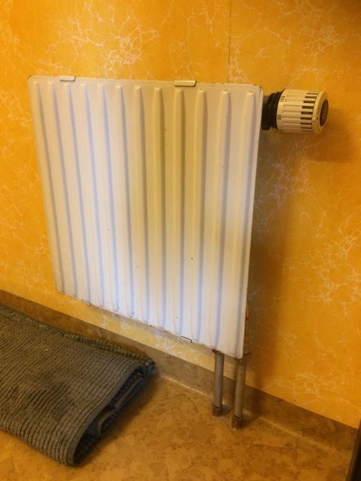 Element med synliga rör som leder upp från golvet mot en handdukstork.