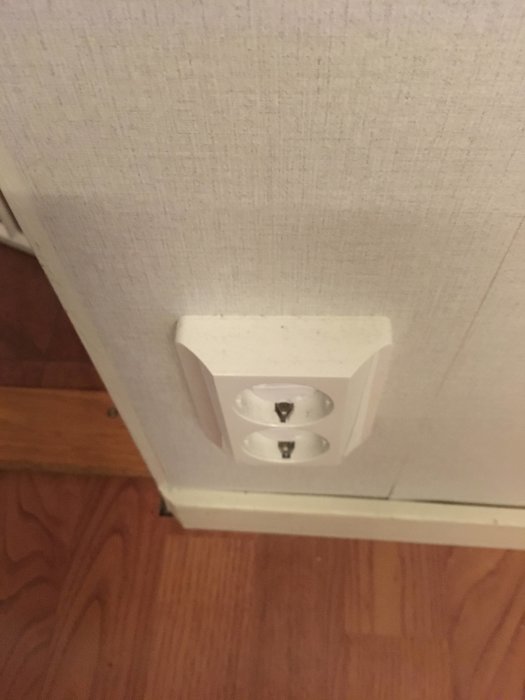 Ett vägguttag med märket "Peha" monterat nära golvet på en tapetserad vägg.