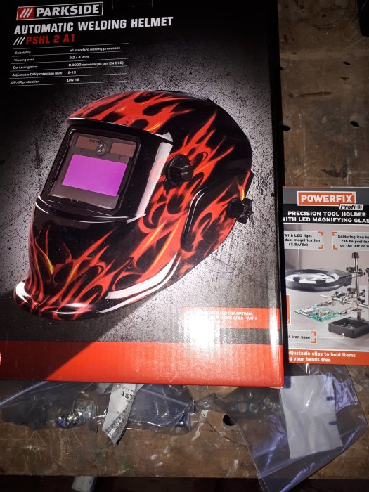 Svetsmask med flamdesign bredvid en förpackning verktygshållare med LED från Lidl.