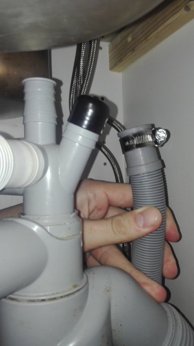 Hand som visar misspassning mellan 25mm diskmaskinens avloppsslang och 20mm avloppsröret under diskhon.