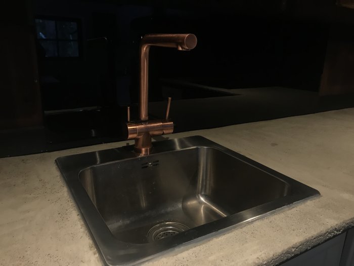 Kök med diskho i rostfritt stål och kran i kopparfinish på bänkskiva.