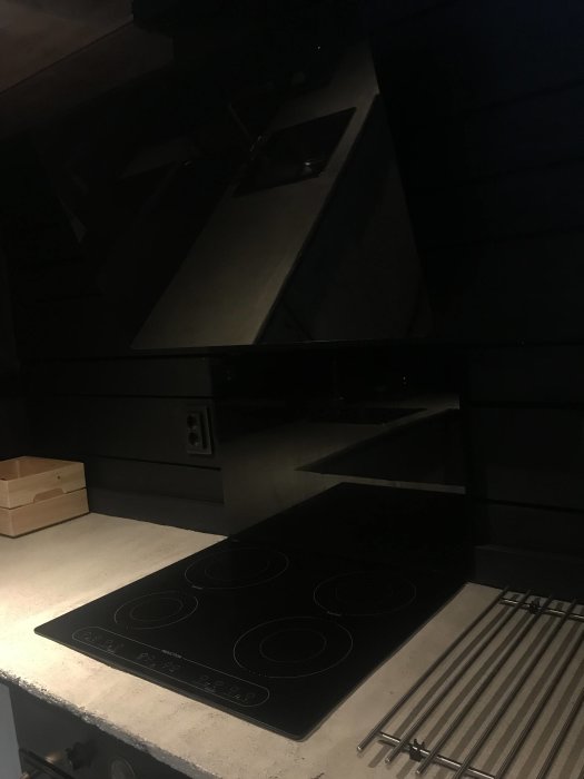 Mörkt kök med svarta skåpluckor, inbyggd ugn och häll, samt en träkryddhylla.