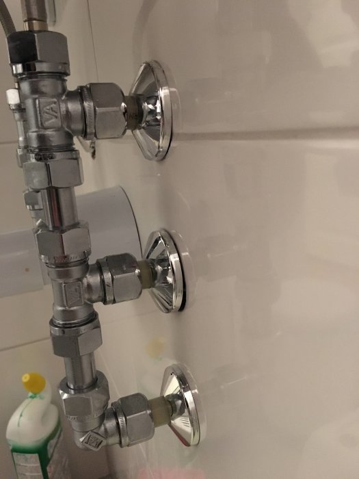 Badrumsvägg med synliga VVS-installationer inklusive rör, kopplingar och väggbrickor.