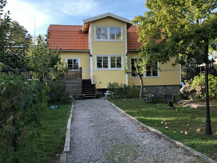 Renoverat gult hus med rött tak och nytt tillägg, omgivet av en trädgård med gräs, träd och utspridda leksaker.