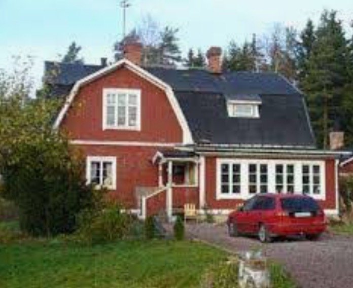 Ett rött hus med svart tak och en röd bil framför, diskussionspunkt om husets hörndesign.