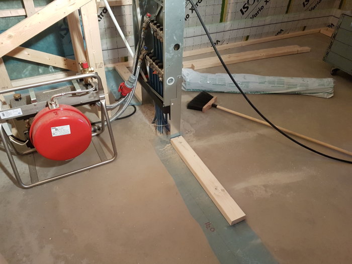 En pågående renovering med värmesystem, isolerad vägg, soppborste och osb-skiva på golvet.