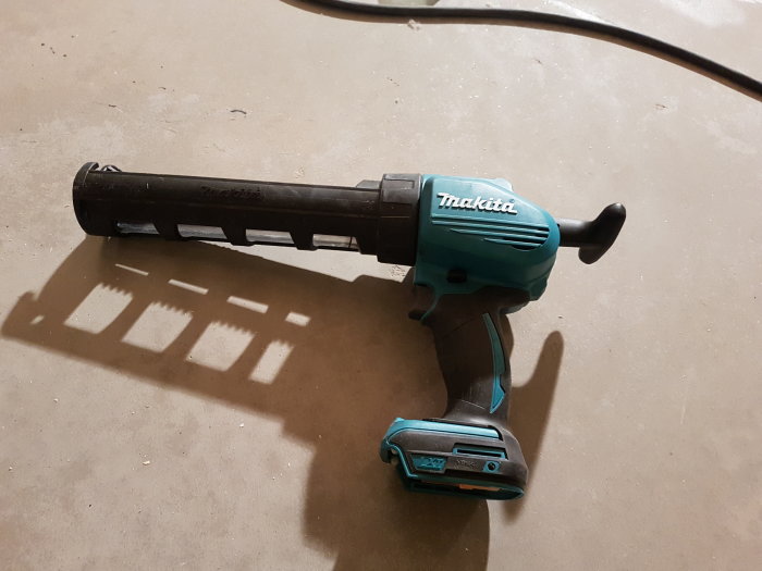 Batteridriven Makita fogpistol på ett betonggolv med dess skugga, använd för tätning i byggprojekt.