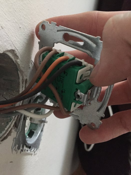 Hand som håller en elektrisk kopplingsdosa med flera ledningar och en grön dimmermodul under installation.