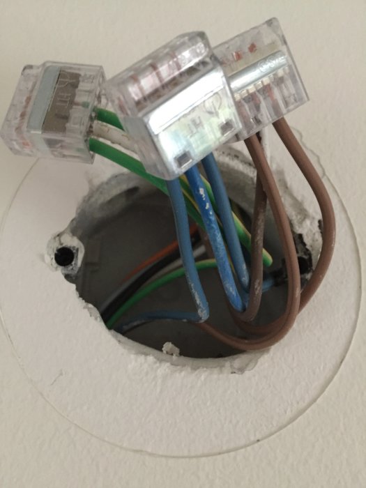 Elektriska kablar och skarvklämmor i en öppen kopplingsdosa på en vägg.