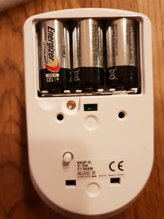 Bakstycket av en larmenhet med batterifack där tre AA-batterier är installerade, CE-märkning synlig.