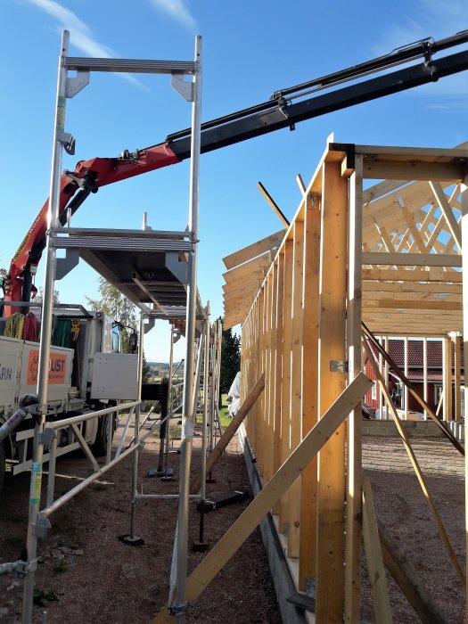 Kranbil hjälper till att resa en träbyggnads stomme med synliga takstolar och skenställning.