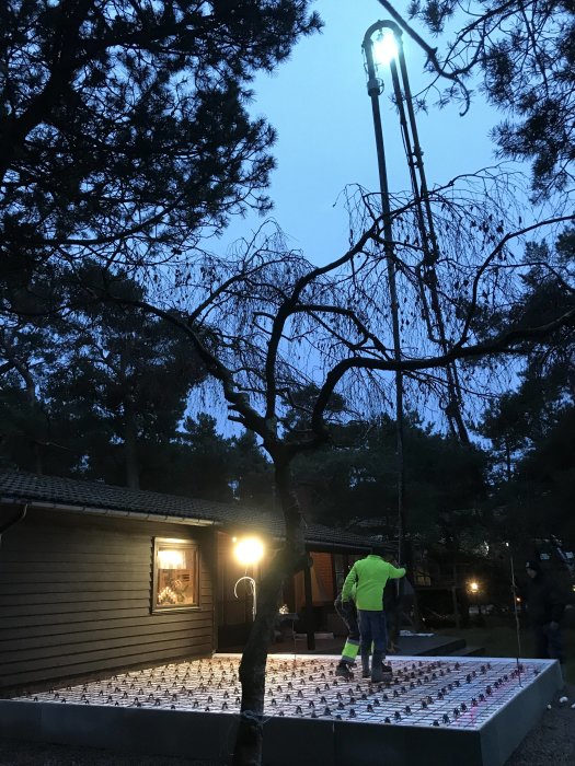 Nylaggd betongplatta med armeringsnät för uterum, arbetare och konstgjort ljus i skymning.