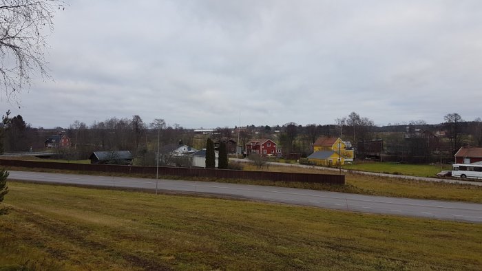 Översikt av igenvuxen tomt med utmärkta gränspinnar, röda huset med buss intill och gult hus.