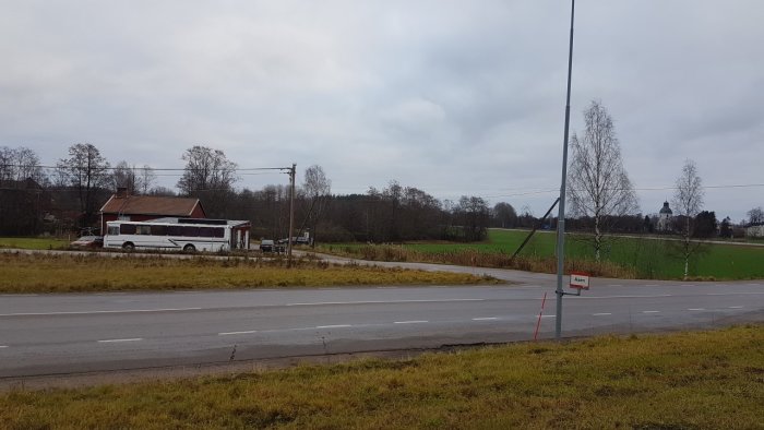 Röd kåk med stor vit buss, igenvuxen tomt, pinnar markerar tänkt byggyta, gult hus till höger.