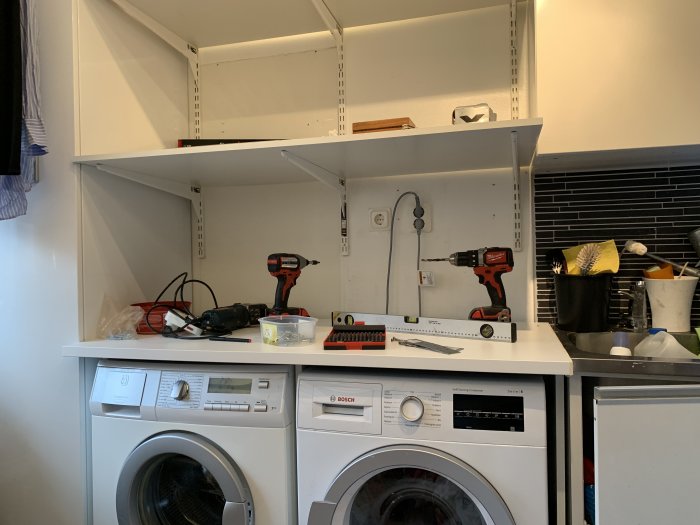 Tvättmaskin och torktumlare under bänkskiva med verktyg och eluttag ovanför.
